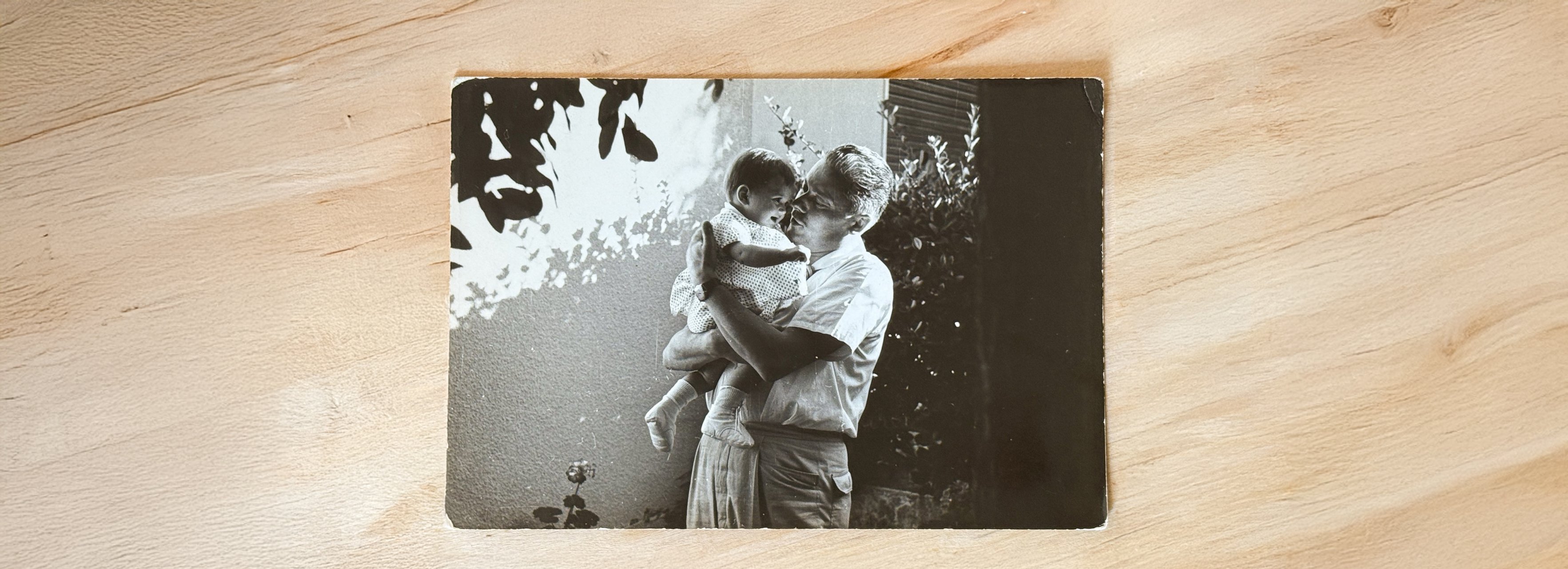 An old black-and-white print lying on a wooden table: a father holding his baby daughter