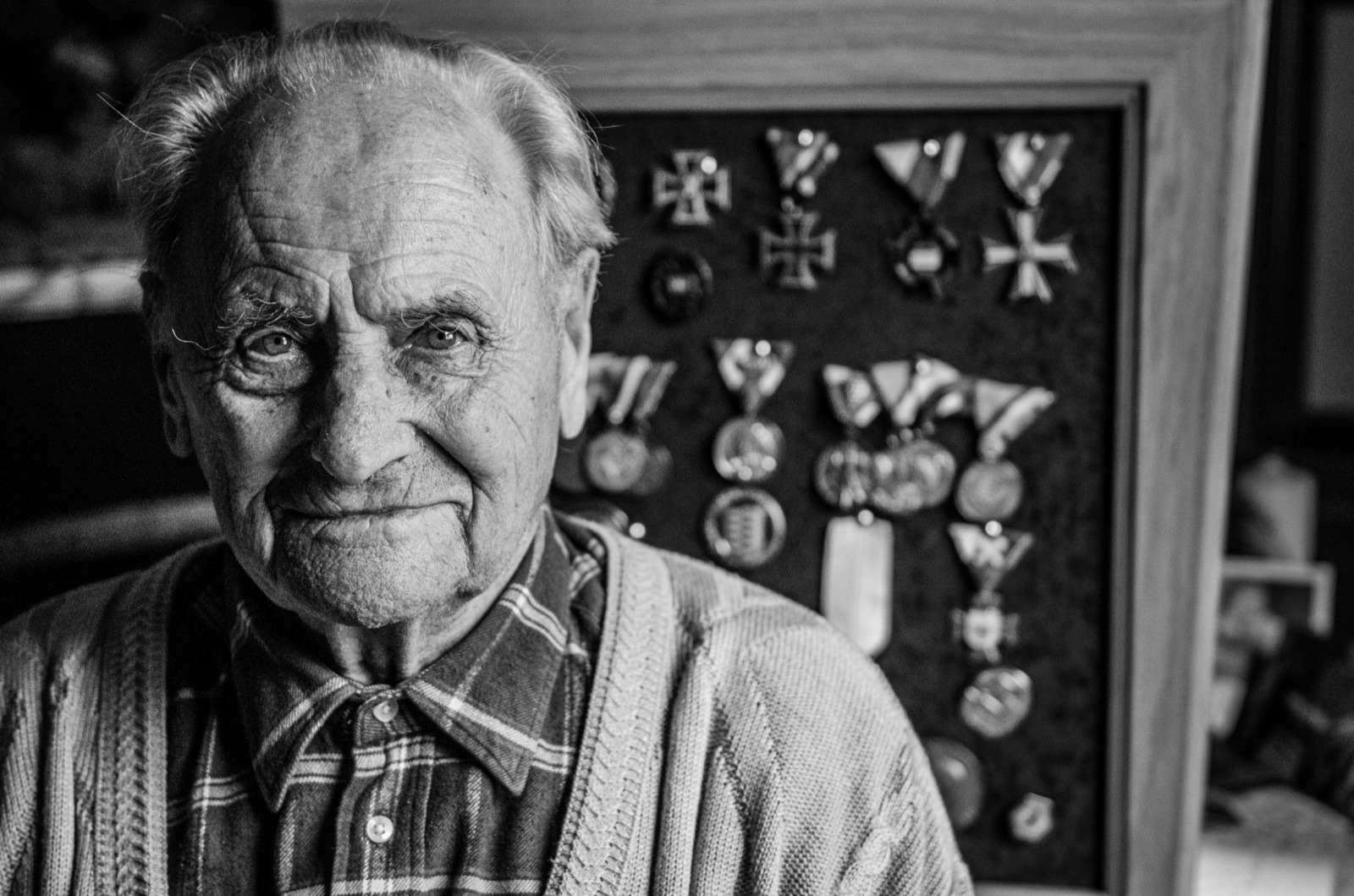 An elderly man beside his framed wall of medals and memories