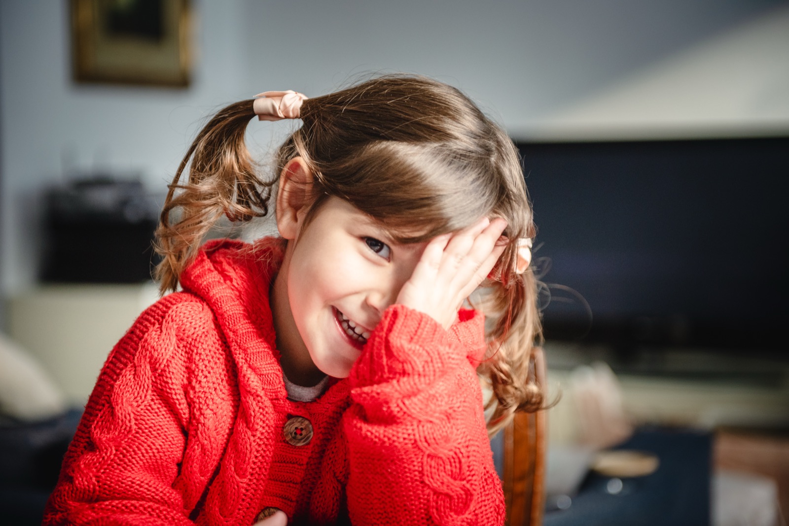 A young girl in a red cardigan laughing at home